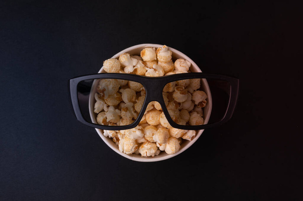 bucket with caramel popcorn and glasses for 3d movies on a black background top view. The concept of a banner or advertising for a cinema. Place for text - 写真・画像