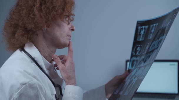 Radiólogo médico mujer caucásica madura examinando tomografía computarizada de pacientes pecho y pulmones en el consultorio del hospital - Imágenes, Vídeo