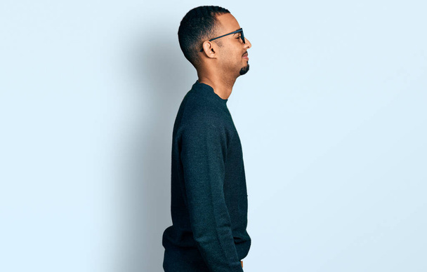 Young african american man wearing casual clothes and glasses looking to side, relax profile pose with natural face with confident smile.  - Photo, Image