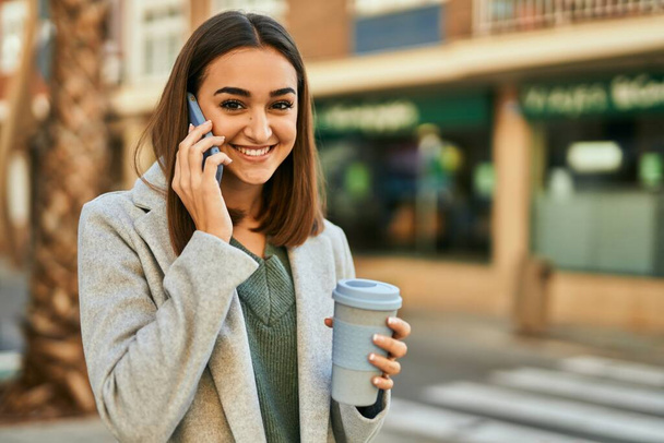 Junges hispanisches Mädchen beim Kaffeetrinken in der Stadt auf dem Smartphone. - Foto, Bild