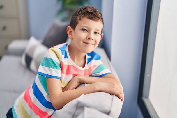 Szőke gyermek mosolyog magabiztos ül kanapén otthon - Fotó, kép