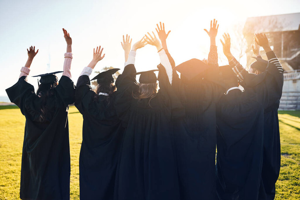 Celebrating warm memories and big dreams for the future. Rearview shot of a group of students standing in a line with their arms raised on graduation day. - 写真・画像