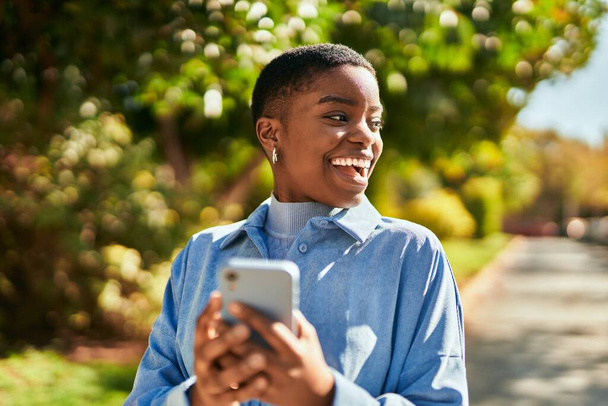 若いアフリカ系アメリカ人の女性が市内のスマートフォンを使って笑顔で - 写真・画像