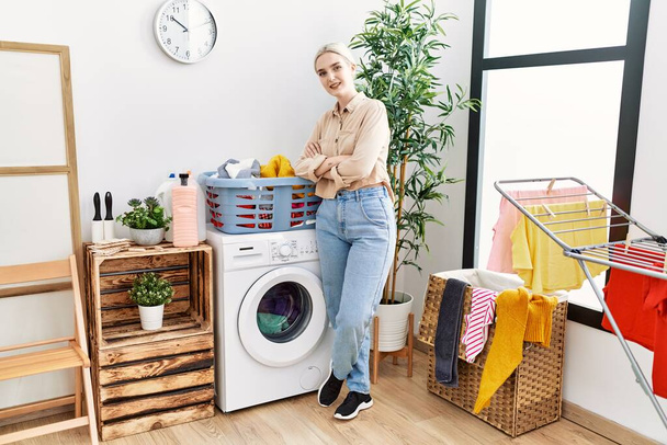 Young caucasian woman smiling confident standing with arms crossed gesture at laundry room - Photo, Image