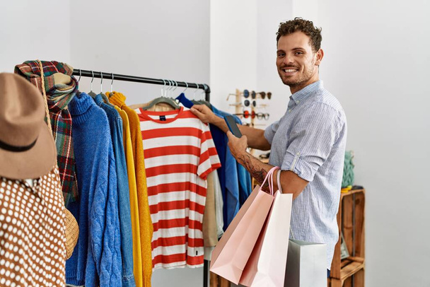 Mladý hispánský zákazník muž usmívá šťastný výběr oblečení v obchodě s oblečením. - Fotografie, Obrázek