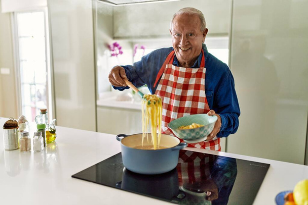 Senior man smiling confident cooking spaghetti at kitchen - 写真・画像