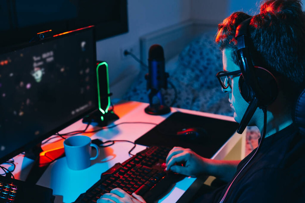 Bilgisayarda oynayan, çevrimiçi video oyunlarına bağımlı genç bir adam. Genç oyuncu renkli ışıklarla aydınlatılmış. - Fotoğraf, Görsel
