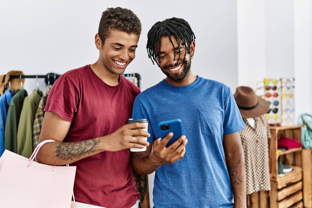 Two men friends holding shopping bags using smartphone at clothing store - Photo, Image