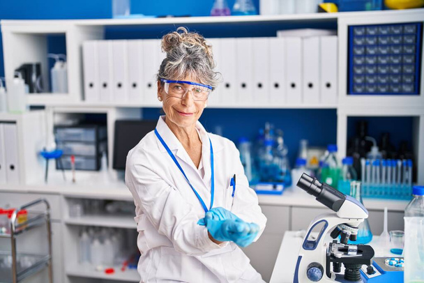 Middle age woman scientist wearing gloves at laboratory - Фото, зображення