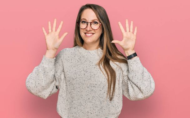 jonge blonde vrouw dragen casual trui en bril tonen en wijzen met vingers nummer tien terwijl glimlachen zelfverzekerd en gelukkig.  - Foto, afbeelding