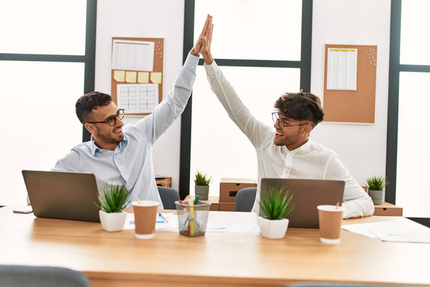Два латиноамериканца, бизнесмены "дай пять" с поднятыми руками, работающие в офисе - Фото, изображение