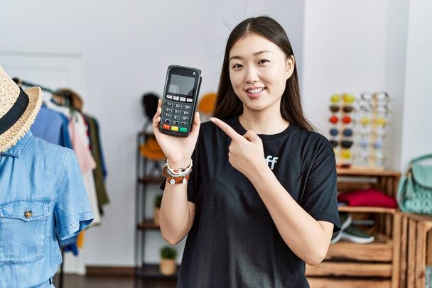 Jeune femme asiatique travaillant comme gestionnaire à la boutique de détail exploitation dataphone souriant heureux pointant avec la main et le doigt  - Photo, image