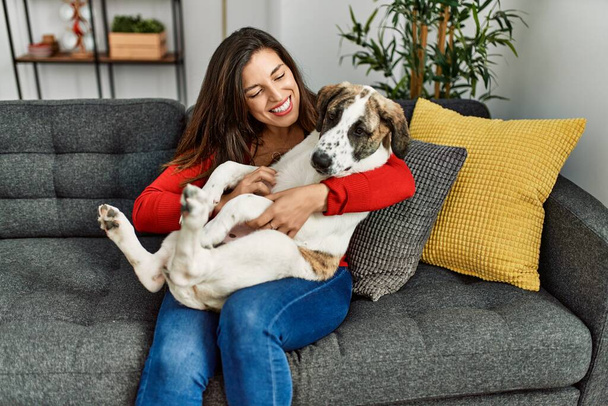 Young woman hugging dog sitting on sofa at home - Φωτογραφία, εικόνα