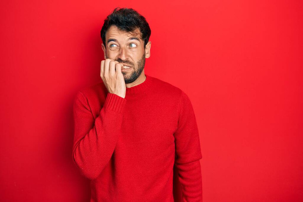 Handsome man with beard wearing casual red sweater looking stressed and nervous with hands on mouth biting nails. anxiety problem.  - Valokuva, kuva