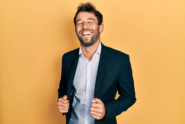 Hombre guapo con barba vistiendo traje de negocios sosteniendo chaqueta sonriendo y riendo en voz alta porque divertido chiste loco.  - Foto, Imagen