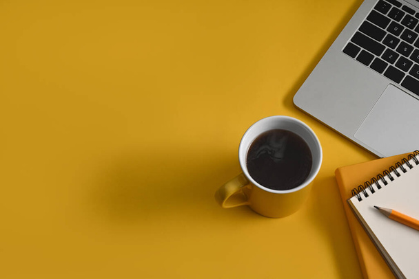 Чашка кофе, ноутбук и ноутбук на желтом фоне с копировальным пространством. - Фото, изображение
