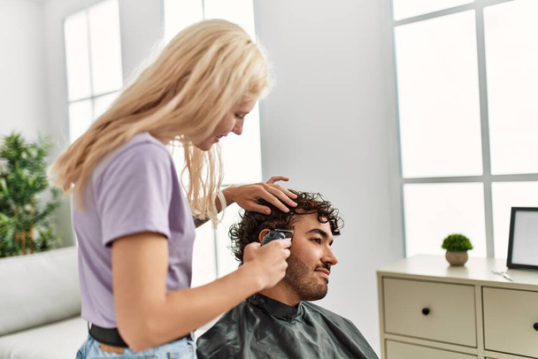 Jeune femme coupe les cheveux à son petit ami à la maison. - Photo, image