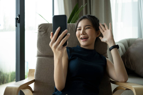 Happy young woman waving hand and enjoying video call with friends via smart phone. - Фото, зображення