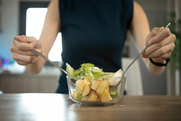 Cropped shot woman mixing fresh healthy vegan salad in glass bowl  in the kitchen at home. - 写真・画像