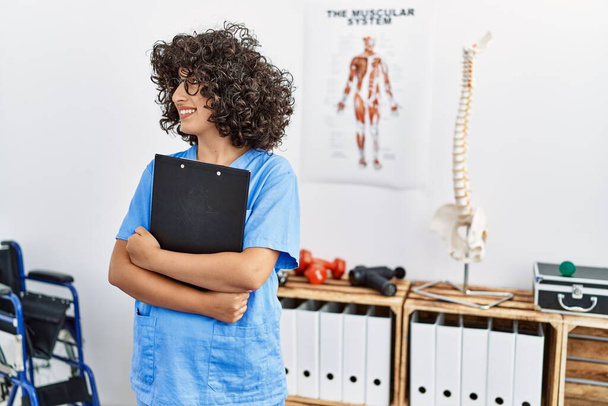 Young middle east woman wearing physio therapist uniform holding clipboard at clinic - Foto, afbeelding