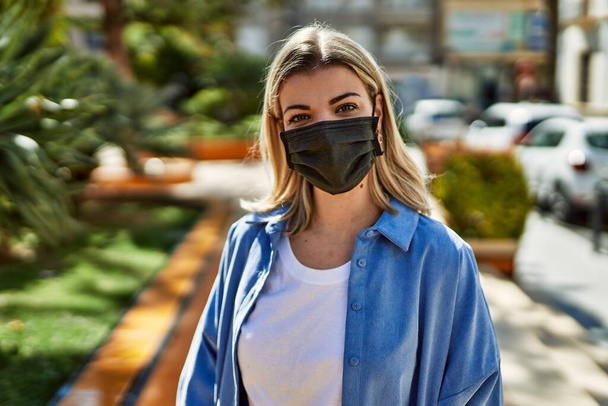 Chica rubia joven con máscara protectora coronavirus de pie en la ciudad. - Foto, imagen
