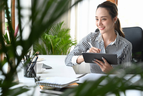 Γοητευτική γυναίκα επιχειρηματίας κάθεται σε άνετο χώρο εργασίας και τη χρήση ψηφιακών tablet. - Φωτογραφία, εικόνα