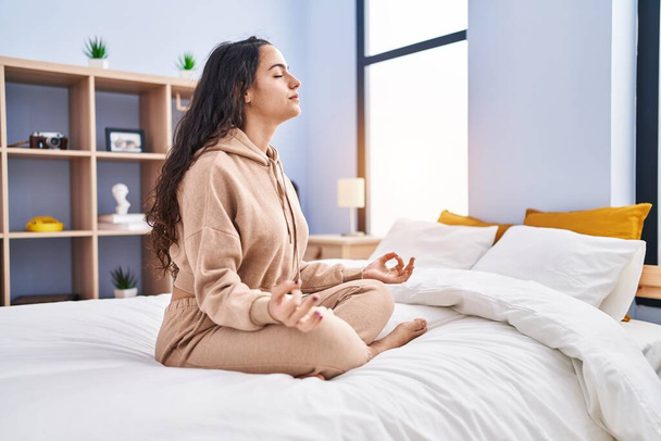 Young hispanic woman doing yoga exercise sitting on bed at bedroom - Photo, Image