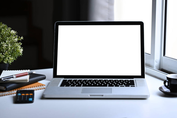 Front view mockup laptop υπολογιστή, φλιτζάνι καφέ, σημειωματάριο και αριθμομηχανή σε λευκό γραφείο. - Φωτογραφία, εικόνα