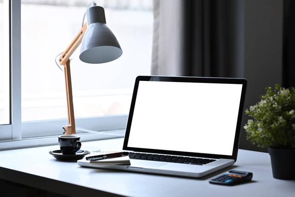 Stylowa przestrzeń robocza z laptopem, lampą, doniczką i filiżanką kawy oraz na białym stole. - Zdjęcie, obraz