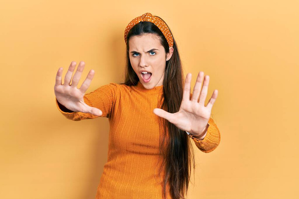 Young brunette teenager wearing casual yellow sweater doing stop gesture with hands palms, angry and frustration expression  - Foto, imagen