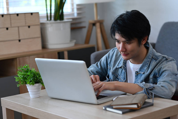 Мужчина, пользуясь услугой интернет-банкинга, ищет информацию на ноутбуке в гостиной. - Фото, изображение