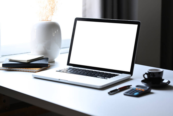Ноутбук-макет с пустым экраном, калькулятор и кофейная чашка на белом столе. - Фото, изображение