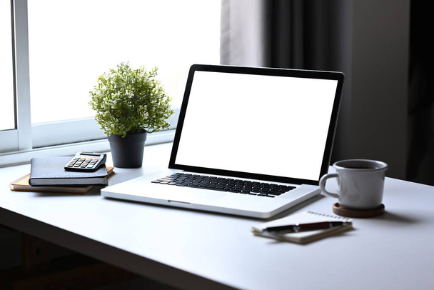 Laptop, Topfpflanze, Kaffeetasse und Notizbücher auf weißem Tisch im hellen Home Office. - Foto, Bild