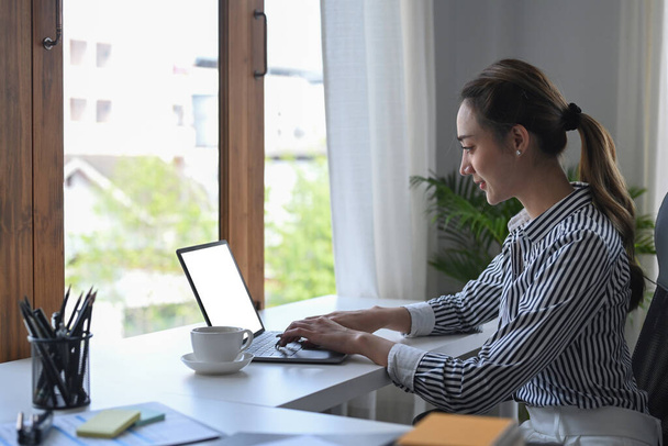 Visão lateral focada trabalhador do escritório do sexo feminino que trabalha com computador portátil no escritório brilhante. - Foto, Imagem