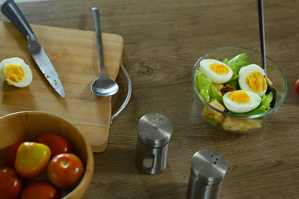 Ahşap masadaki cam kasede haşlanmış yumurta ile vejetaryen salatanın üstünde. Sağlıklı gıda konsepti. - Fotoğraf, Görsel