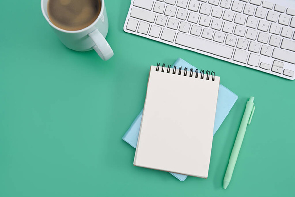 Empty notepad, coffee cup and wireless keyboard on green background. Flat lay. - Φωτογραφία, εικόνα