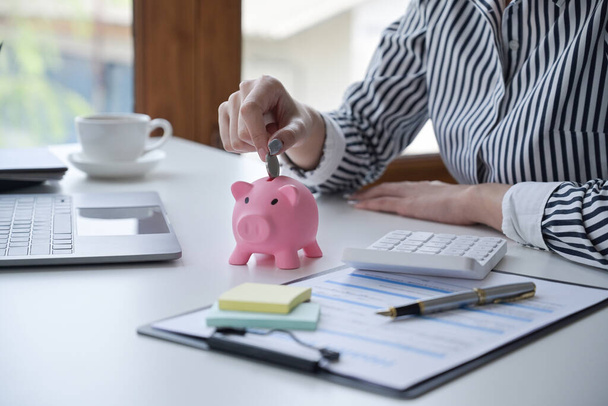 Woman hand putting coin into piggy bank. Saving money, banking, economy concept. - 写真・画像