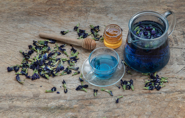 Butterfly pea tea (Clitoria) or Organic blue anchan in Teapot and glass cup served with honey on Old wooden background. Healthy detox herbal drink, Selective focus. - Fotó, kép