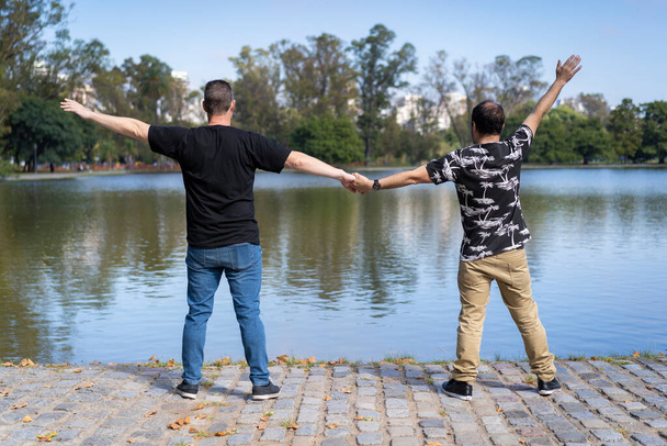 Homosexual white male couple holding hands back to back at a lake - Foto, Imagem