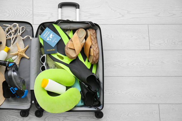 Valise avec accessoires de plage féminins, passeport immunitaire et masque de plongée avec tuba sur fond de bois blanc - Photo, image