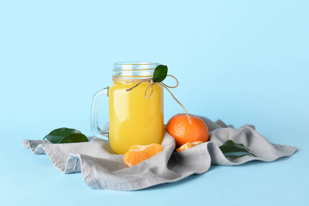 Mason jar of fresh tangerine juice on blue background - 写真・画像