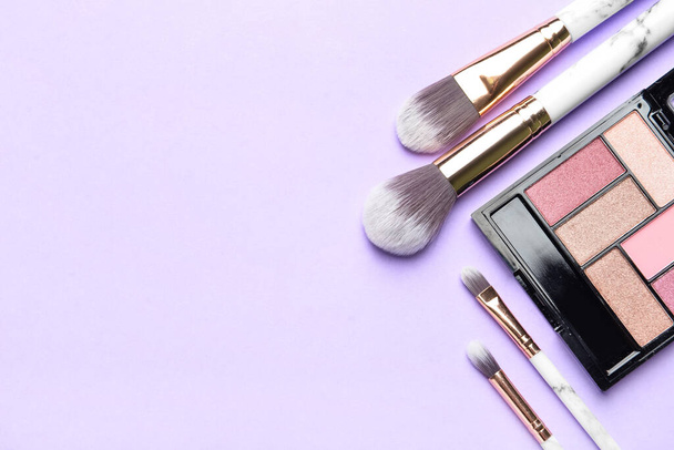 Makeup brushes and eyeshadows on purple background - Photo, Image