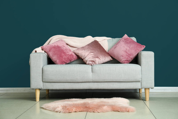 Modernes Sofa mit Kissen und Teppich in der Nähe der Farbwand im Zimmer - Foto, Bild