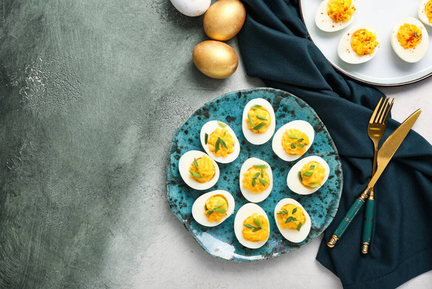 Тарелки с фаршированными яйцами, столовые приборы и салфетки на фоне гранжа. Пасхальный праздник - Фото, изображение