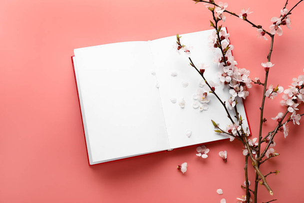 Beautiful blooming spring branches and open notebook with blank pages on pink background, top view - Foto, imagen