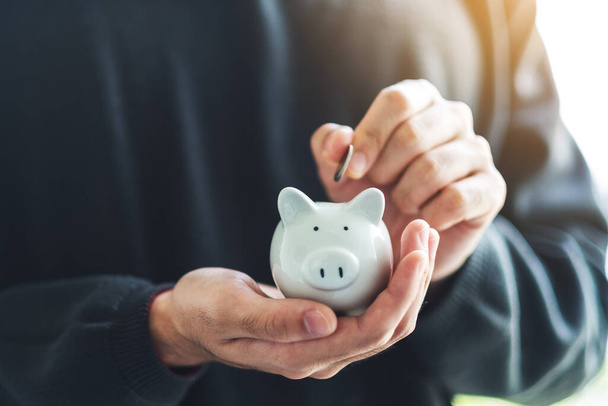 Closeup image of a man holding and putting coin into piggy bank for saving money and financial concept - Photo, Image