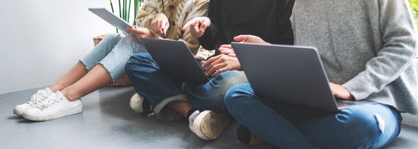 Un grupo de jóvenes sentados y usando un ordenador portátil y una tableta digital juntos - Foto, Imagen