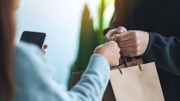 Una mujer que sostiene el teléfono móvil y recibe bolsas de la compra forman el hombre de entrega - Foto, imagen