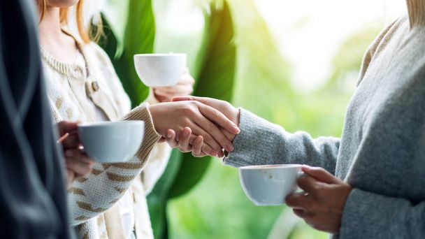 Closeup image of two people holding hands while drinking coffee together - Фото, изображение