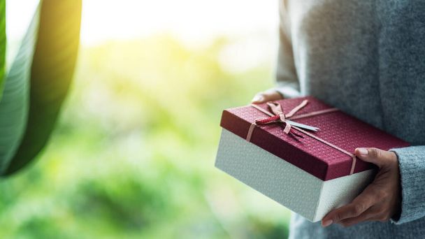 Closeup image of a woman holding a red present box with blurred nature background - Foto, imagen